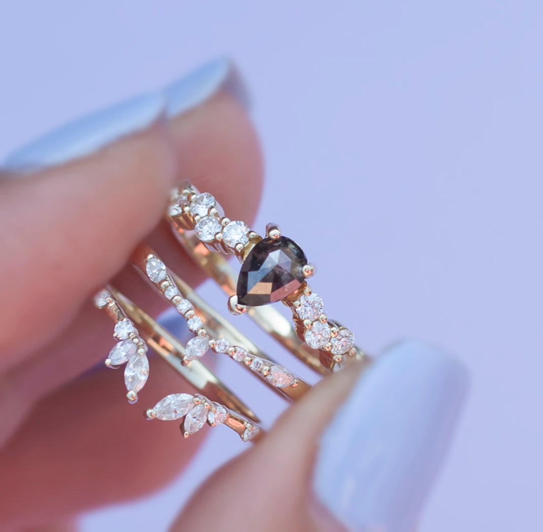 Load image into Gallery viewer, Hand holding the salt and pepper intertwine ring and two white diamond stacking bands close up with a purple background.
