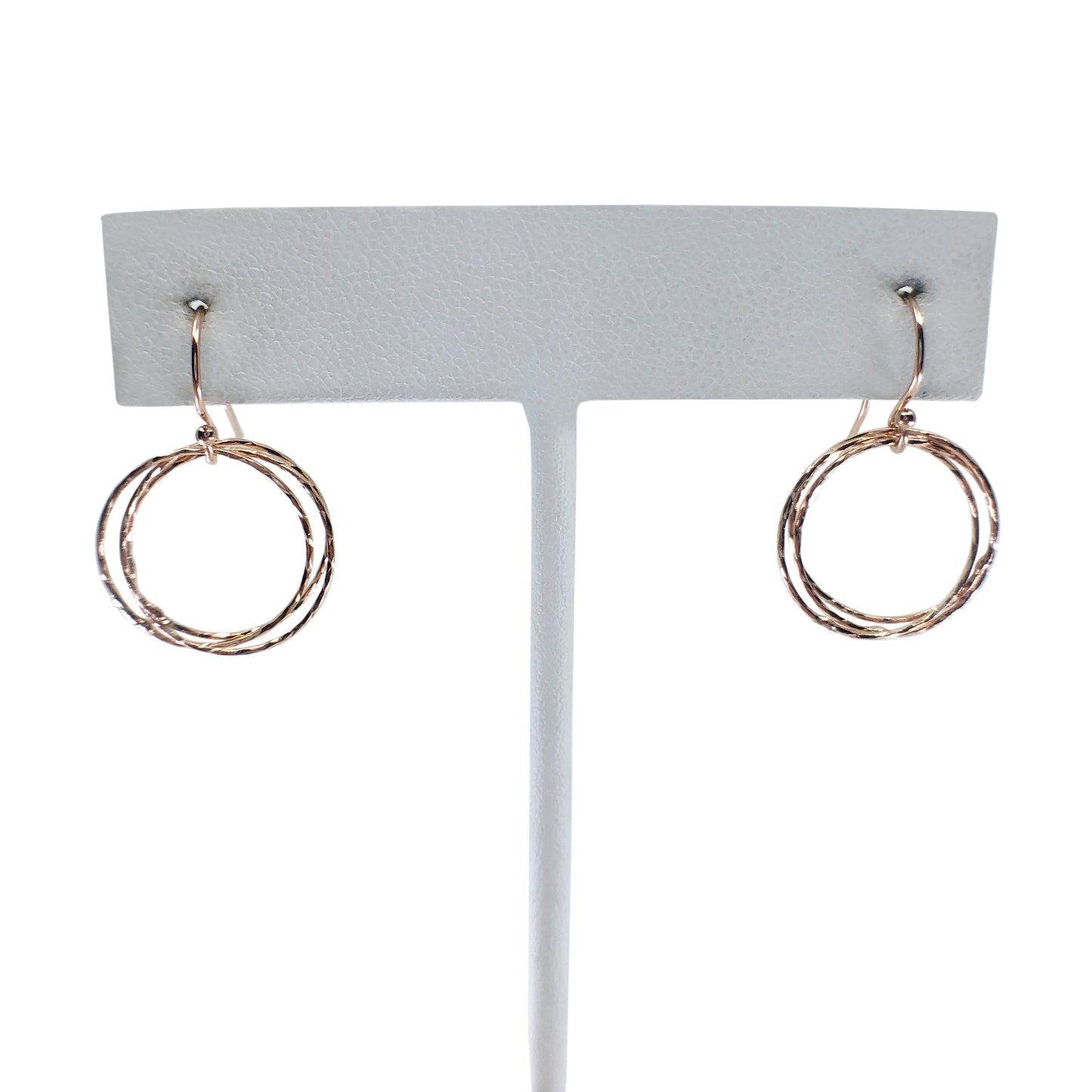 Gold triple circle earrings on earring stand with white background.
