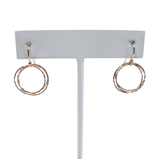 Gold triple circle earrings on earring stand with white background.