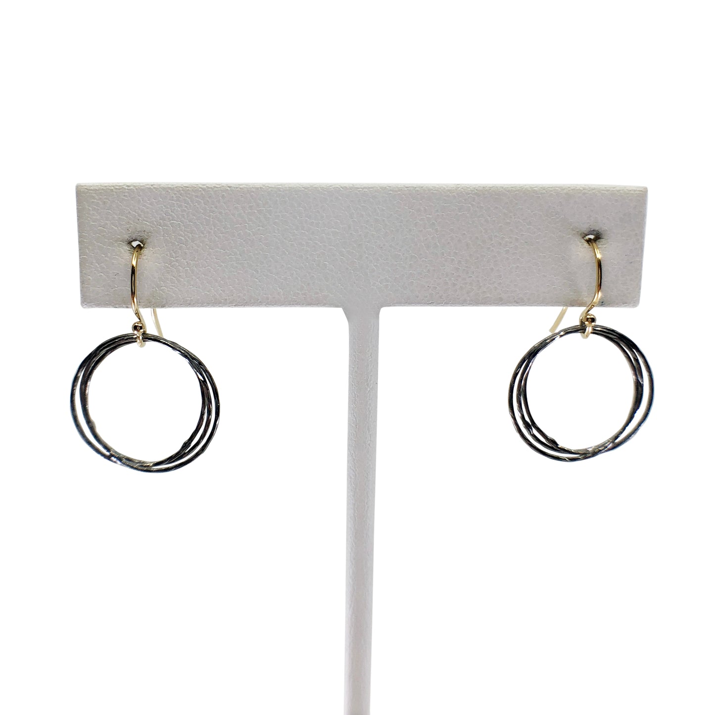 Oxidized silver and gold triple circle earrings on earring stand with white background.