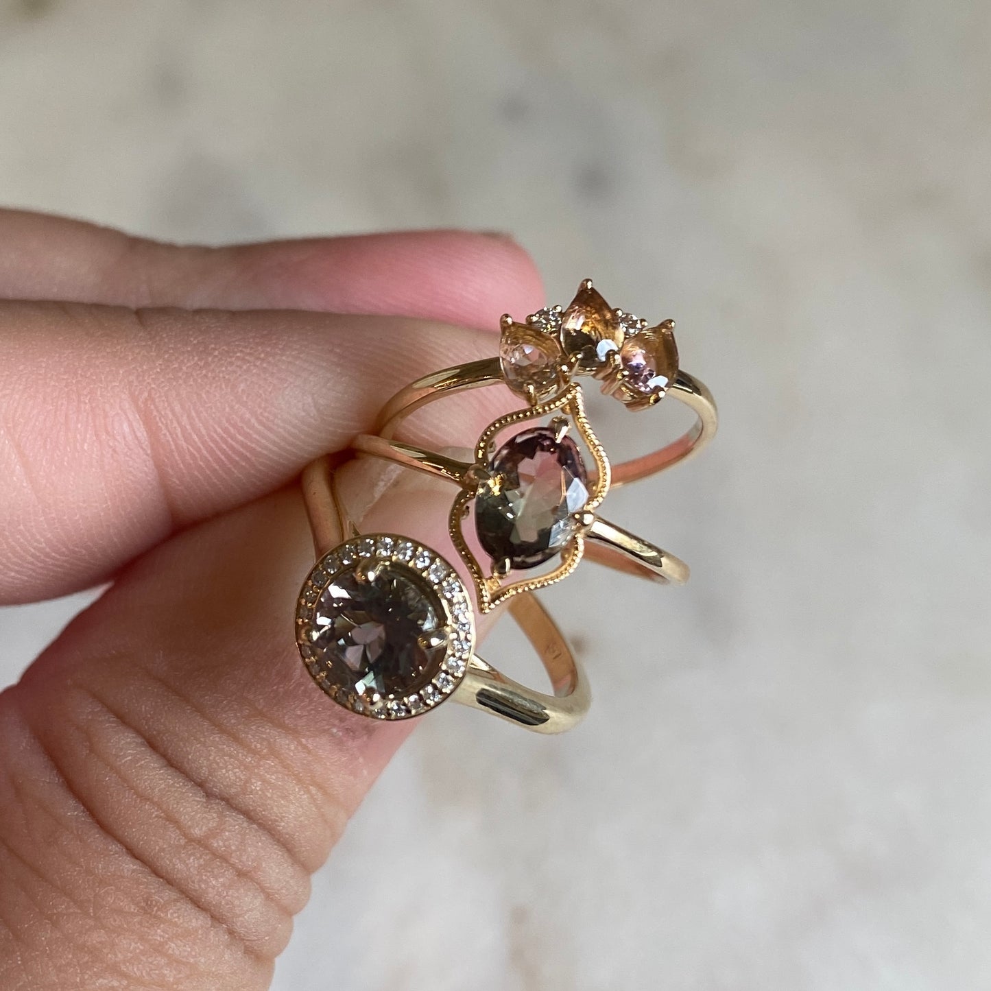 hand holding the sunstone diamond halo ring with two other rings 