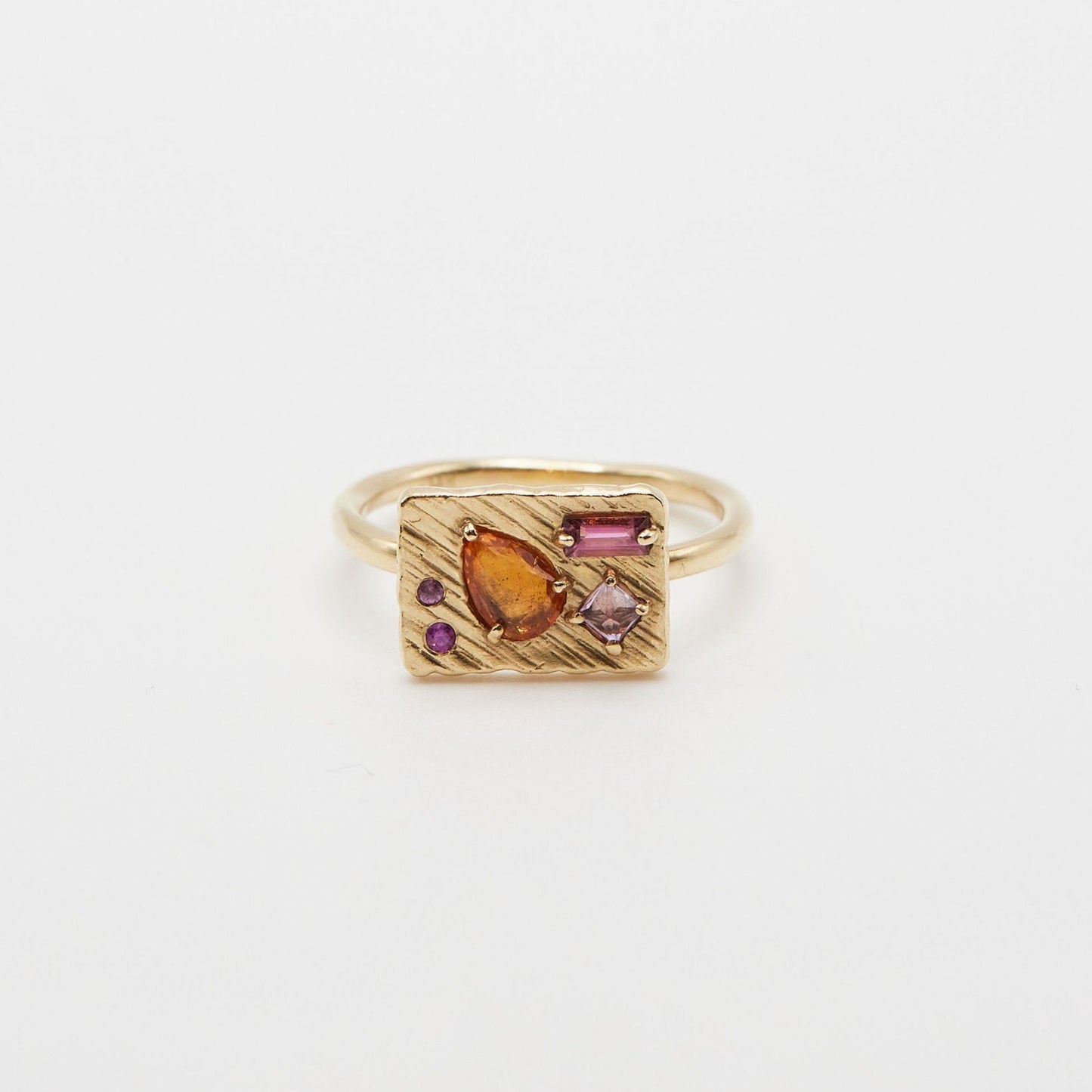 rectangle shaped gold ring with orange pear shaped stone, rectangle pink stone, and three round pink stones on white background