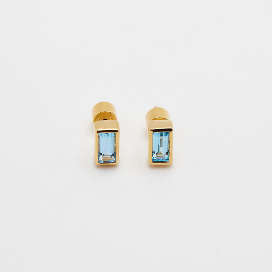 gold bezel set stud earrings with rectangle shaped blue topaz on white background