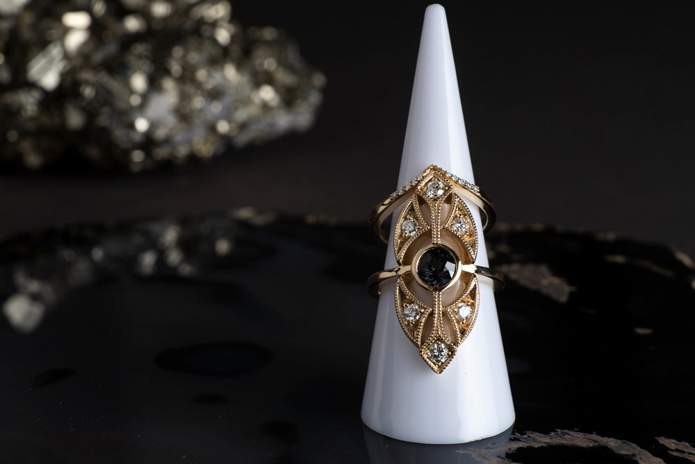 Grey spinel ring in yellow gold photographed on a ring cone with a black agate background