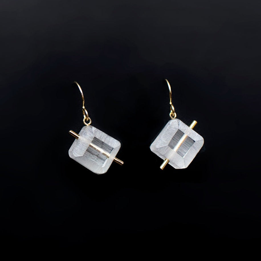Load image into Gallery viewer, White acrylic cubes with a gold bar dangle earrings on black background.
