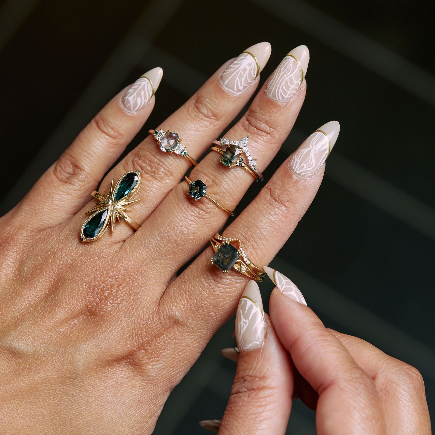 close up of a model wearing the spinel lilac oval ring on the upper knuckle of her ring finger with a large ring on her lower ring finger, three rings on her middle finger, and two rings on her ring finger, with a black tile background