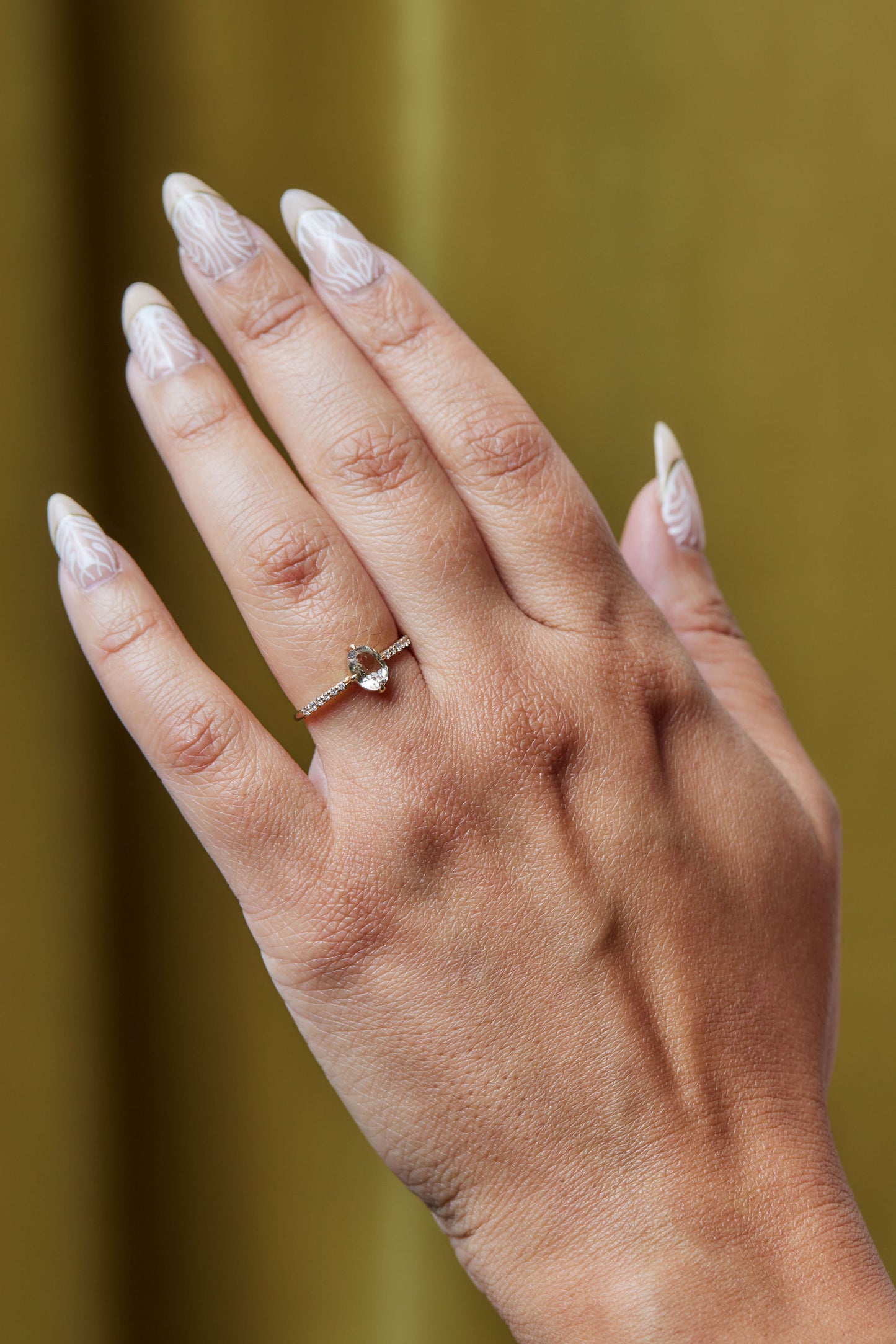 a model wearing the crystal tourmaline solitaire ring on her left ring finger with a velvet chartreuse colored backdrop 