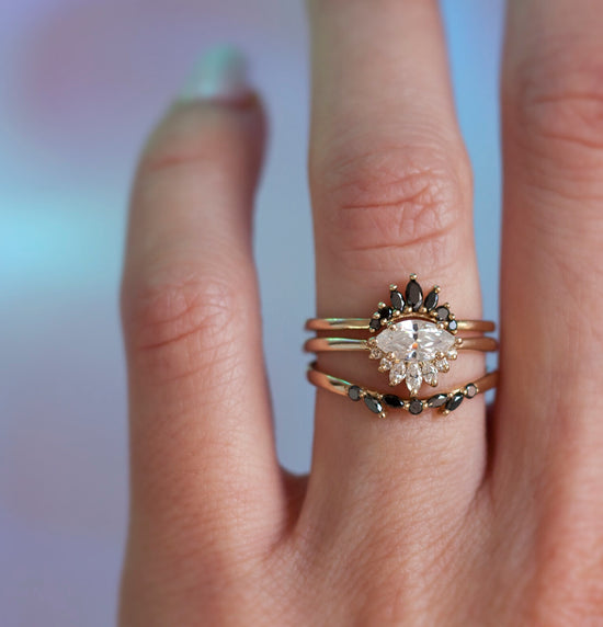 White diamond sideways set marquise ring with diamond crown, stacked on hand with two black diamond bands.