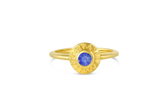 18k yellow gold sunburst circle ring with blue sapphire center stone on white background.