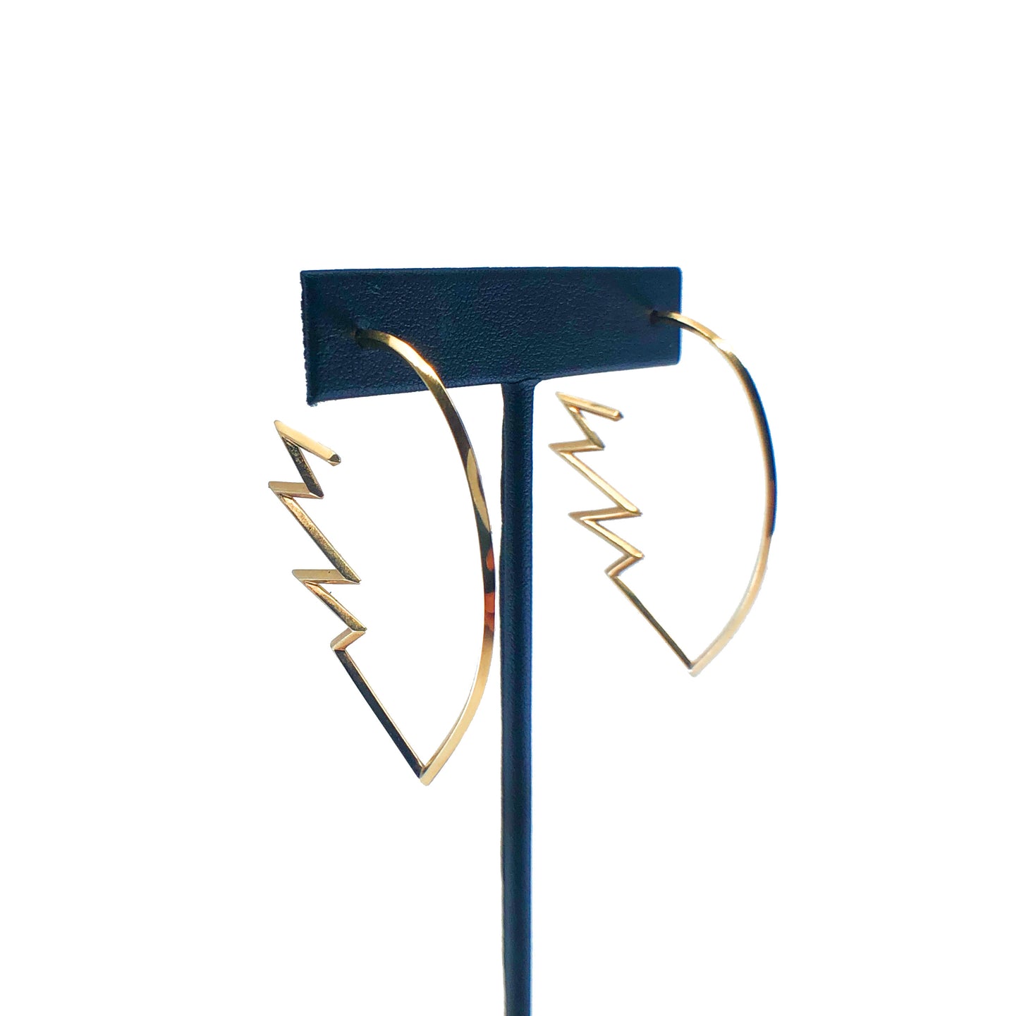 Gold zig zag hoop earrings on earring stand with white background.