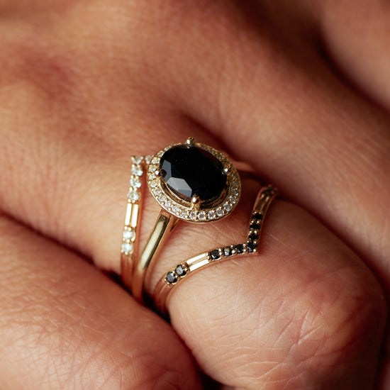 Madison Ave Ring with onyx center stone and diamond halo stacked with two diamond V shaped bands on hand.