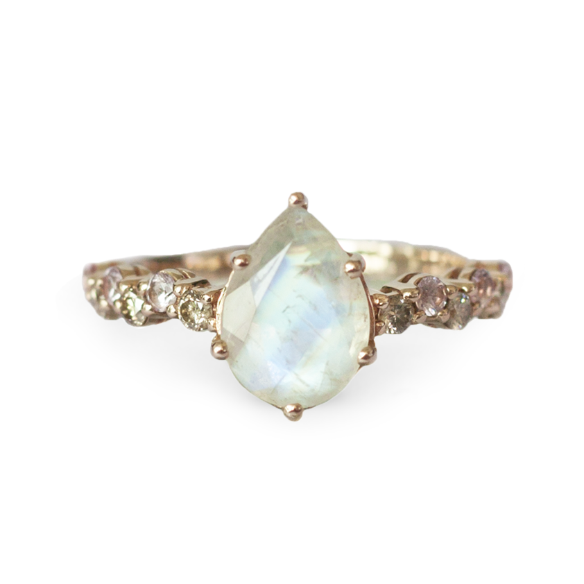 Pear shaped rainbow moonstone set on a sapphire and champagne diamond bluster band, close up on white background.