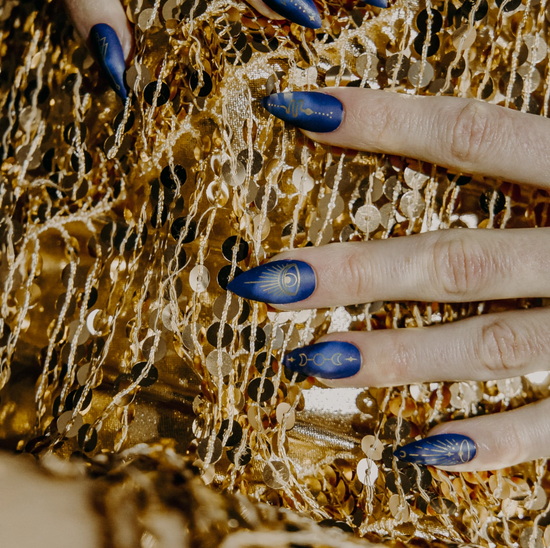 Hand modeling blue and gold celestial design press on nails on gold sequin background.