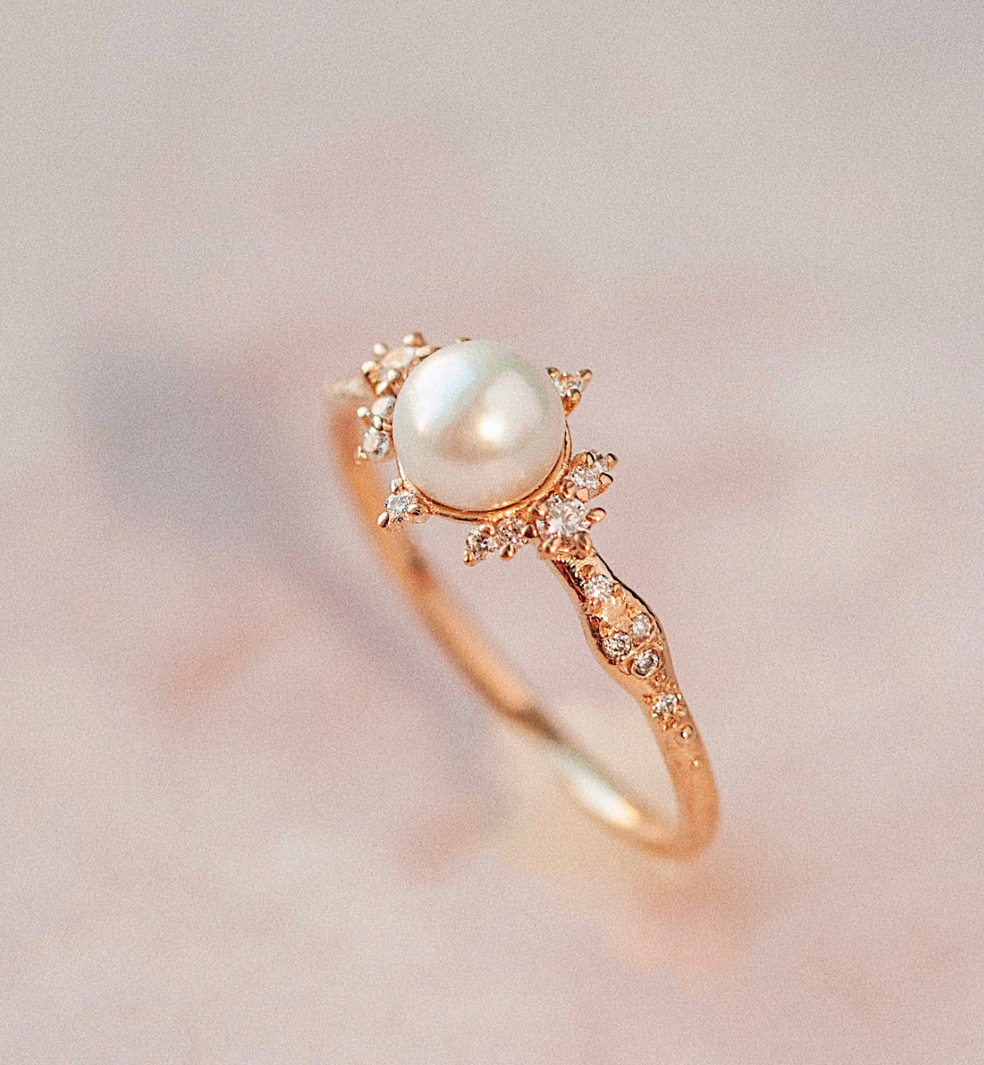 Side view of pearl and diamond ring on light pink background.
