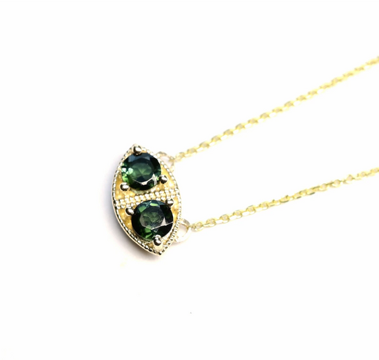 a marquise shaped pendant necklace with two round bi color green sapphires stones and milgrain details close up on a white background