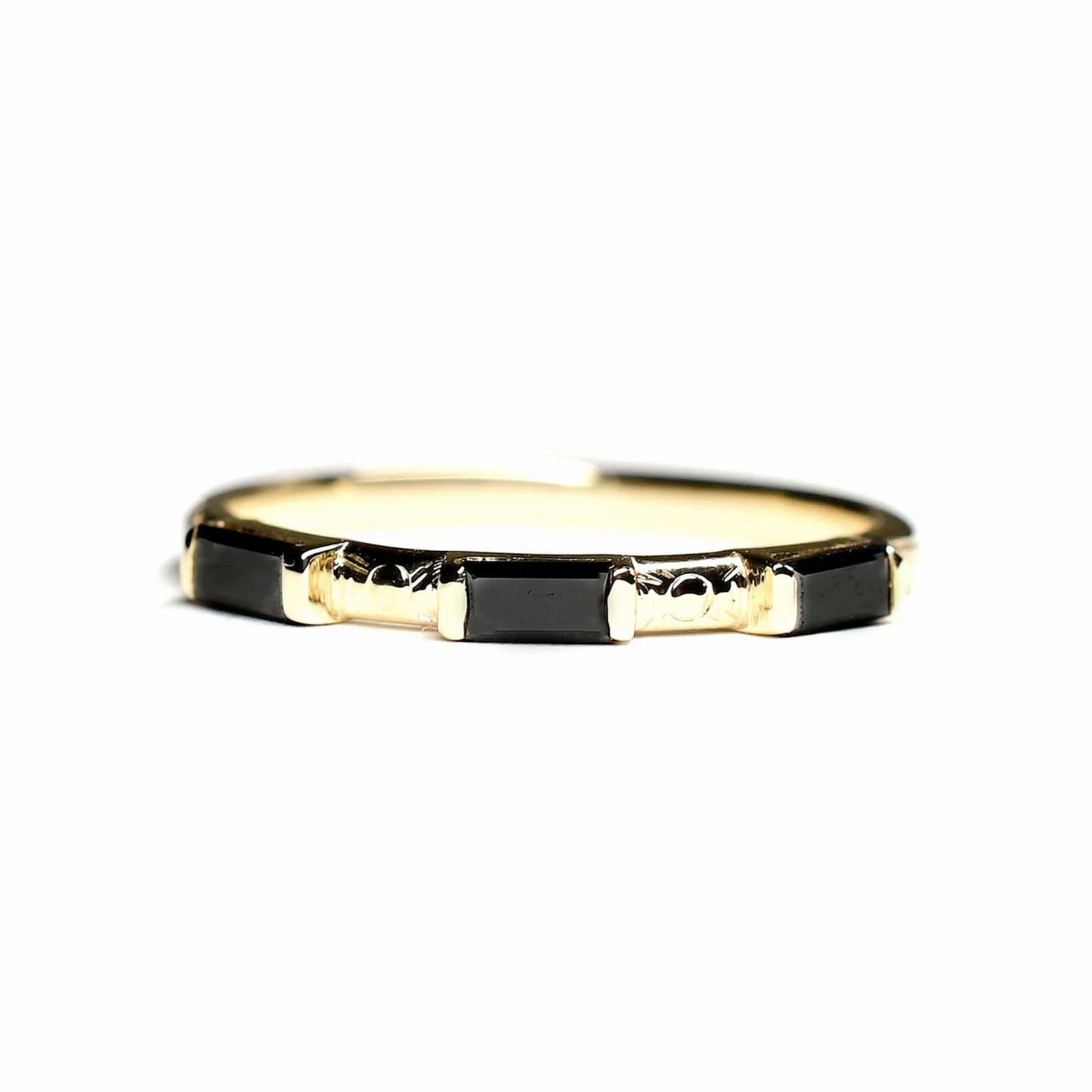 a 14k yellow gold ring with three black diamond baguettes with hand engraved details on a white background