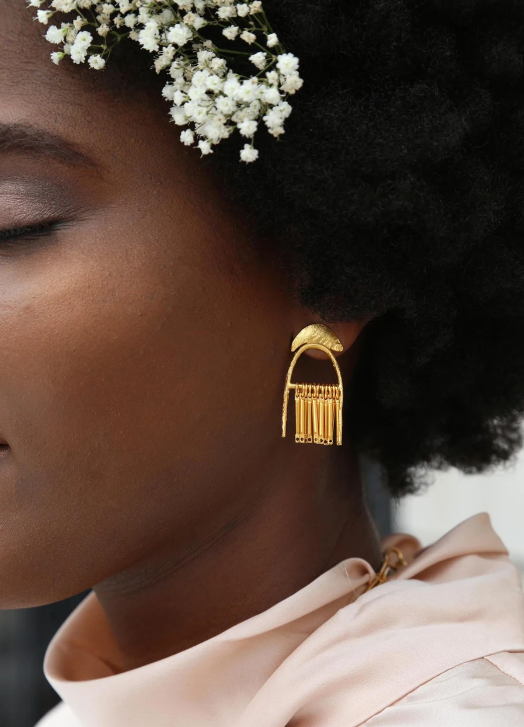 1.5 inches long, brass dangle earrings in gold beign worn by woman in pink blouse and flowers in her hair, pictured from a side angle in front of a white background 