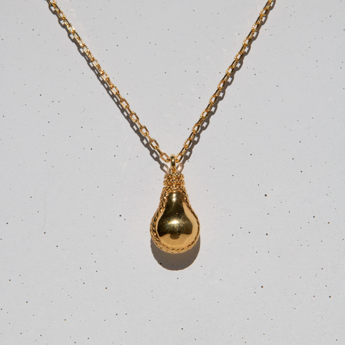 gold lightbulb shaped pendant on grey speckled background