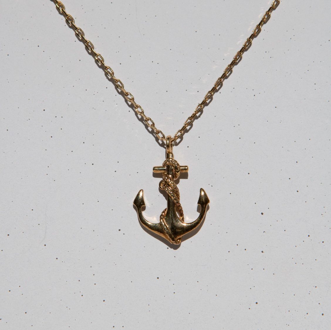 gold anchor shaped pendant necklace on grey speckled background