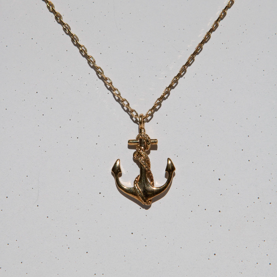 gold anchor shaped pendant necklace on grey speckled background