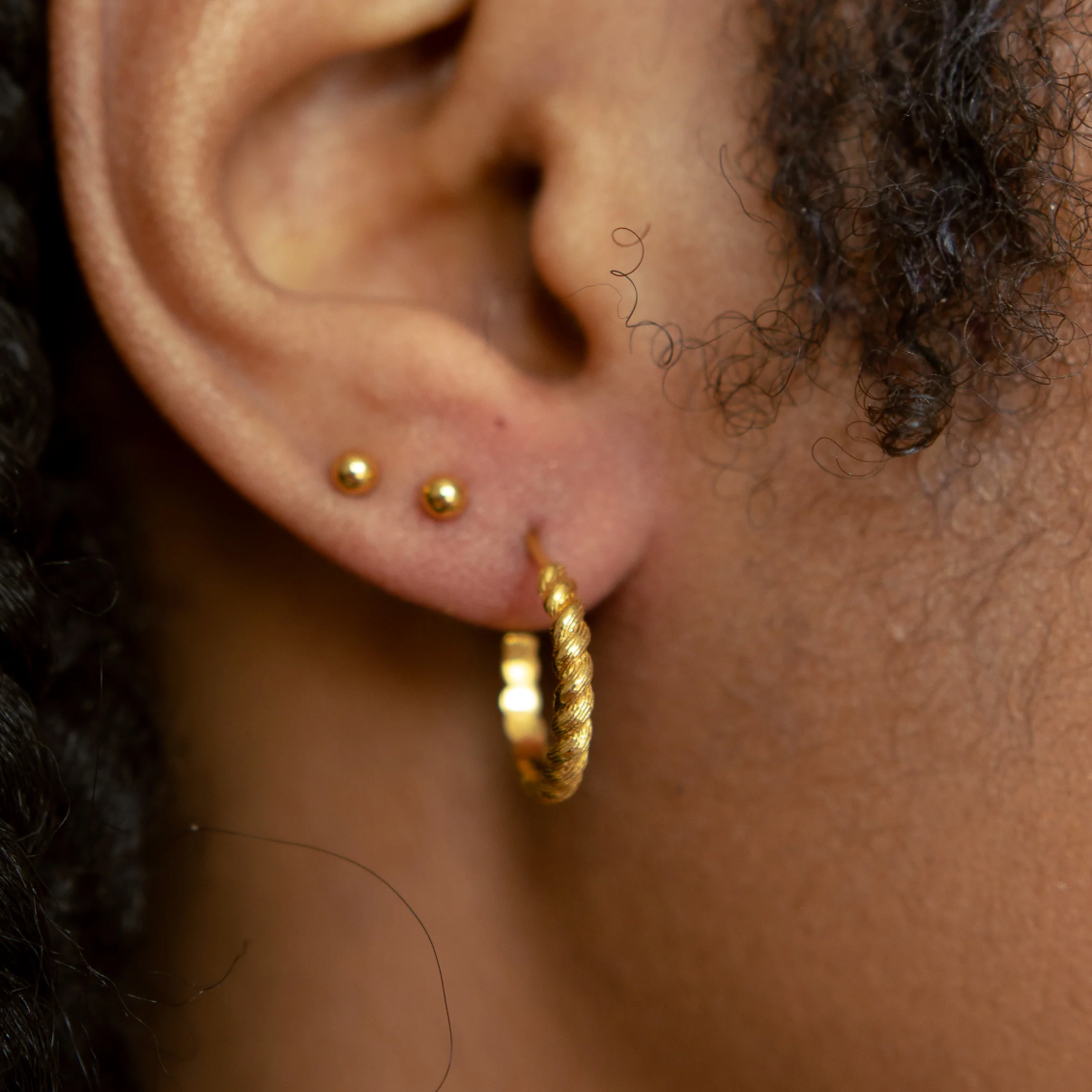close up of model wearing the gold braided hoops earrings with two tiny gold circle stud earrings