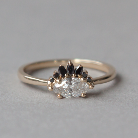 Marquise diamond set sideways on white gold band with black diamond crown, close up on grey background.
