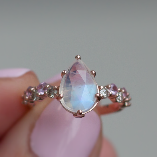 Hand holding pear shaped rainbow moonstone intertwine ring and a morganite and diamond marquise ring, close up.