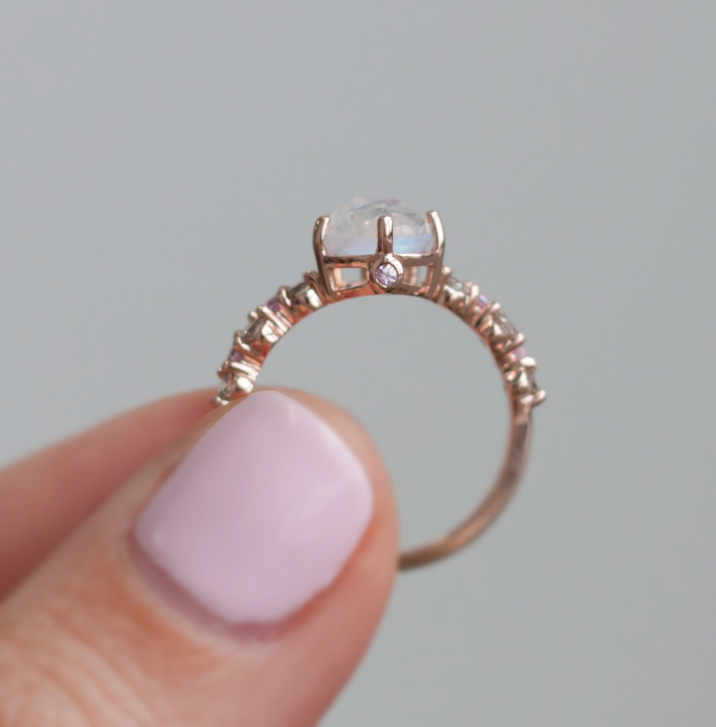 Side view of rainbow moonstone intertwine ring close upon grey background.
