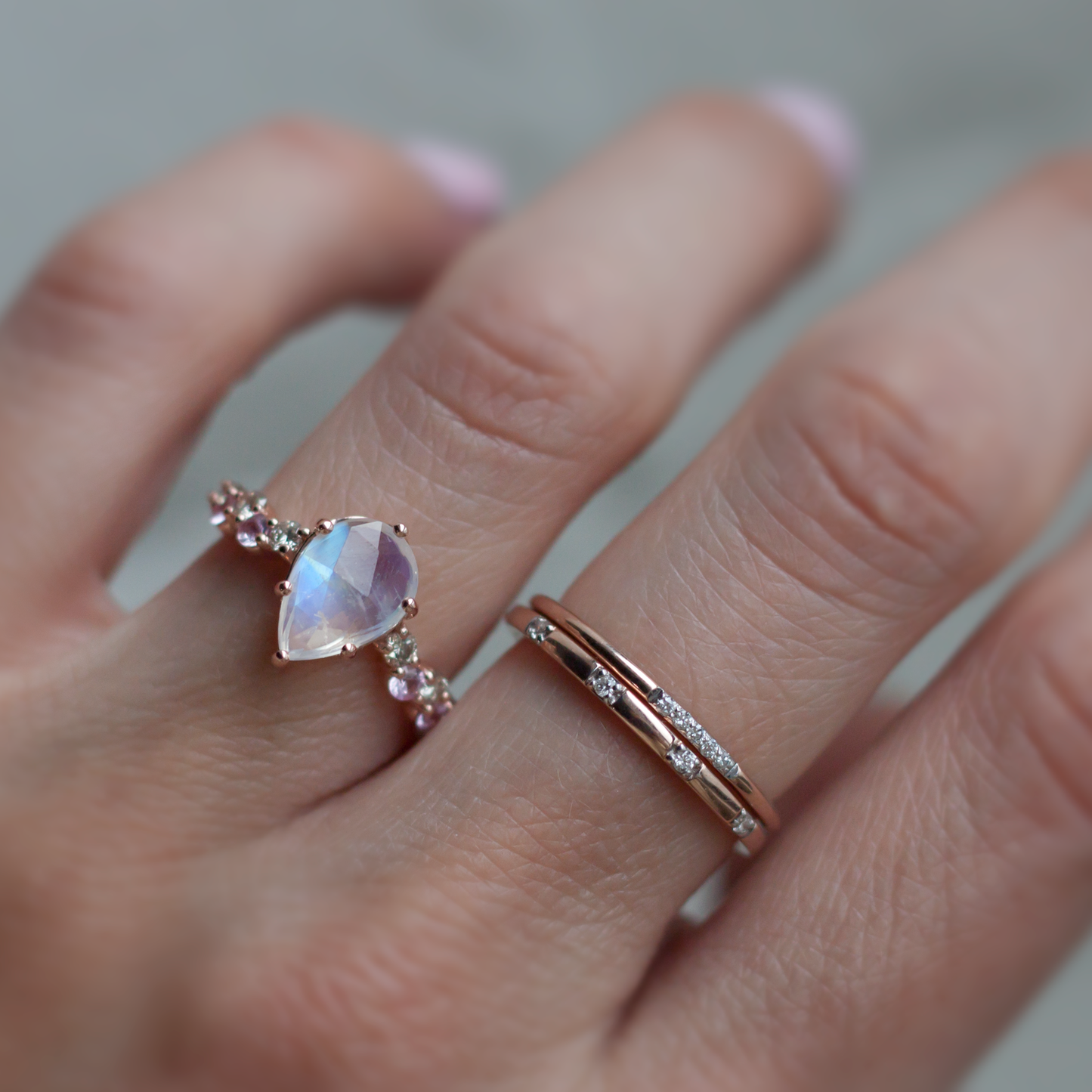 Hand modeling pear shaped rainbow moonstone intertwine ring and two diamond stacking bands.