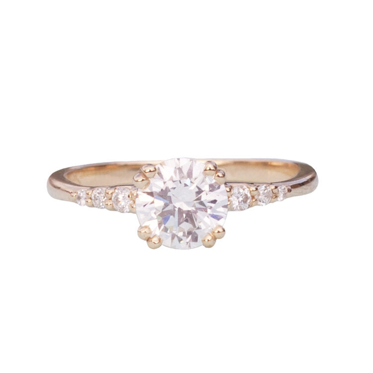 Round diamond solitaire ring with diamond accents on the band, close up on white background.