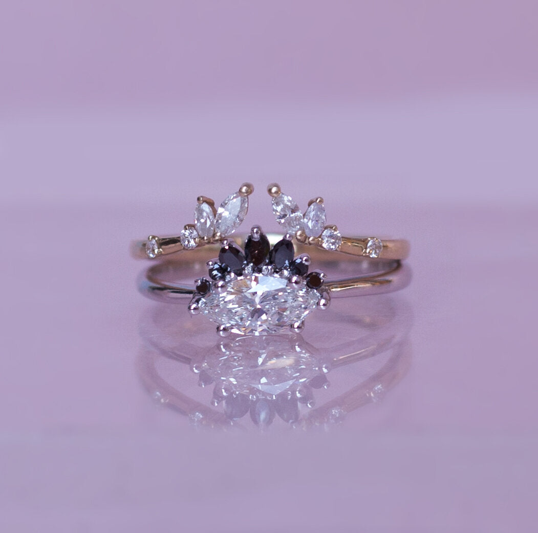 Marquise diamond set sideways on white gold band with black diamond crown, stacked with an open diamond band on purple background.