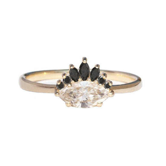 Marquise diamond set sideways on gold band with black diamond crown, close up on white background.
