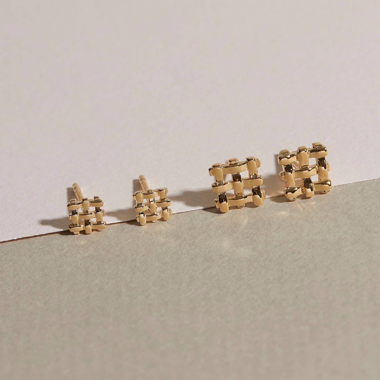 the small and mini crosshatch stud earrings on a beige background