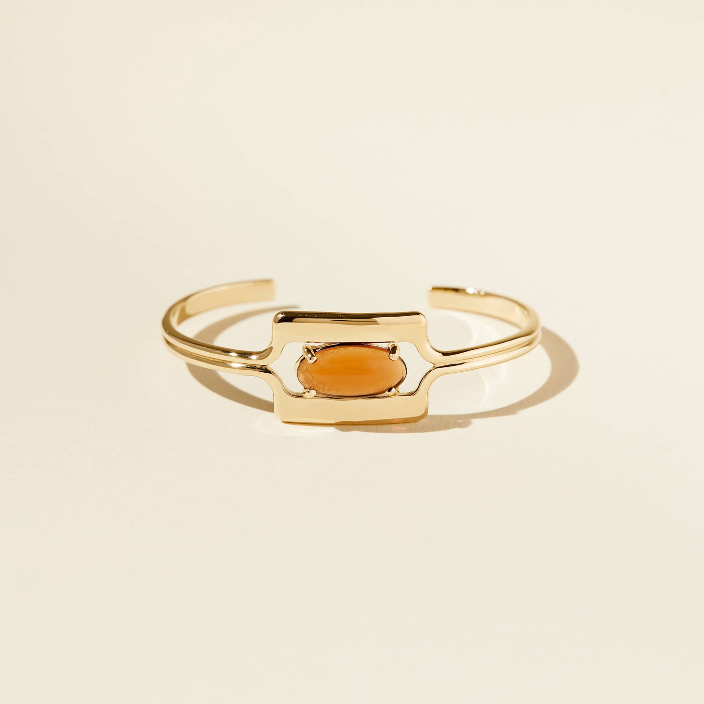 front view of the walton cuff bracelet with an amber brown glass cabochon on a beige background